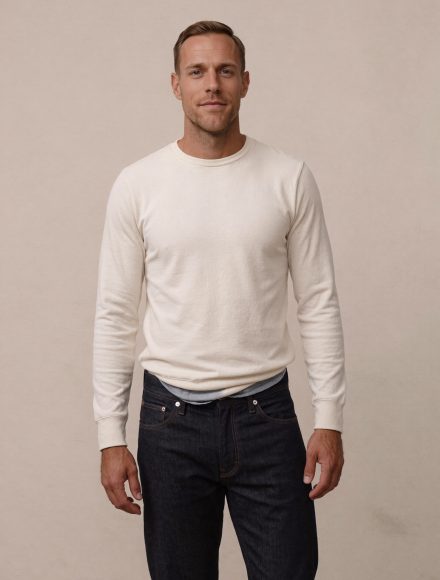 Tall man in an off-white knit and dark indigo jeans, waistband sitting low on the hips showing insufficient rise