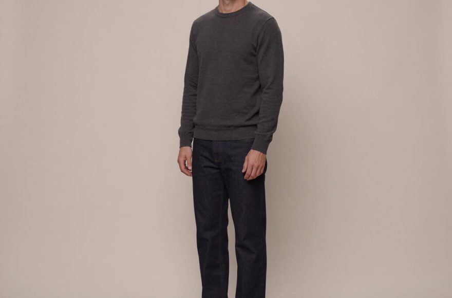 A tall man in a charcoal sweater and dark denim wearing slim low-profile sneakers