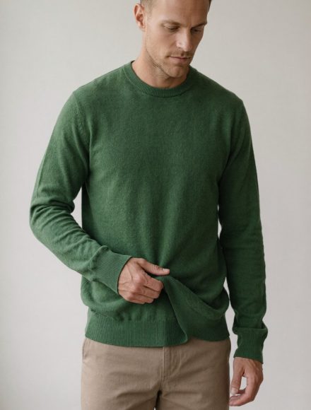 Tall man pinching a fold of excess fabric at the side of an oversized forest green sweater
